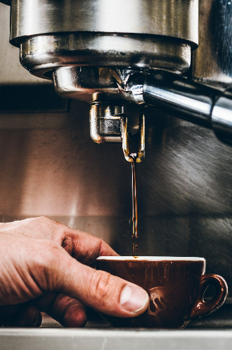 jak parzyć caffe latte - Męska dłoń trzyma filiżankę i napełnia ją kawą.